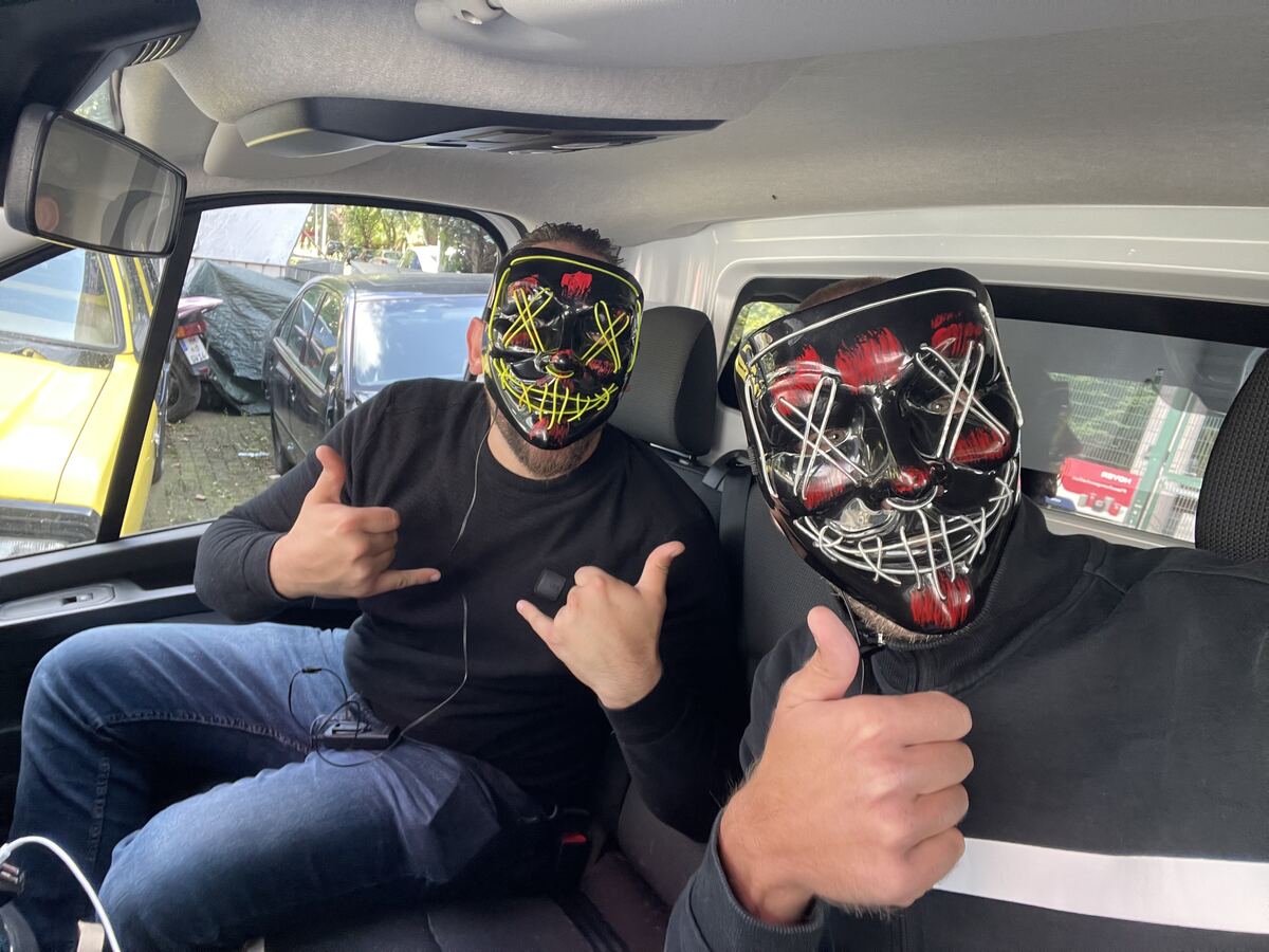 Two people wearing glowing LED masks on the back seat of a car